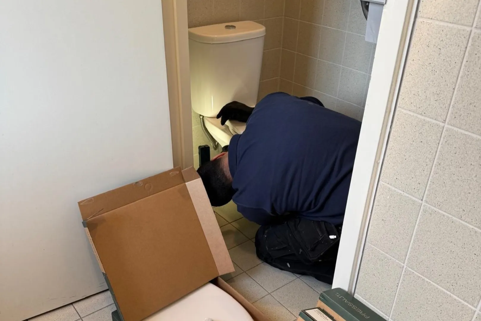 Loodgieter hurkt bij een toilet voor onderhoud en reparatie.